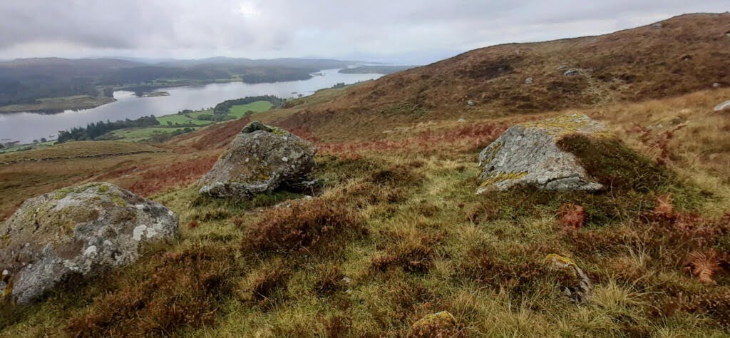 Open hillside with boulders in the foreground and a loch in the background