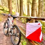 Bike against a bridge edge with a white and orange orienteering flag in the foreground
